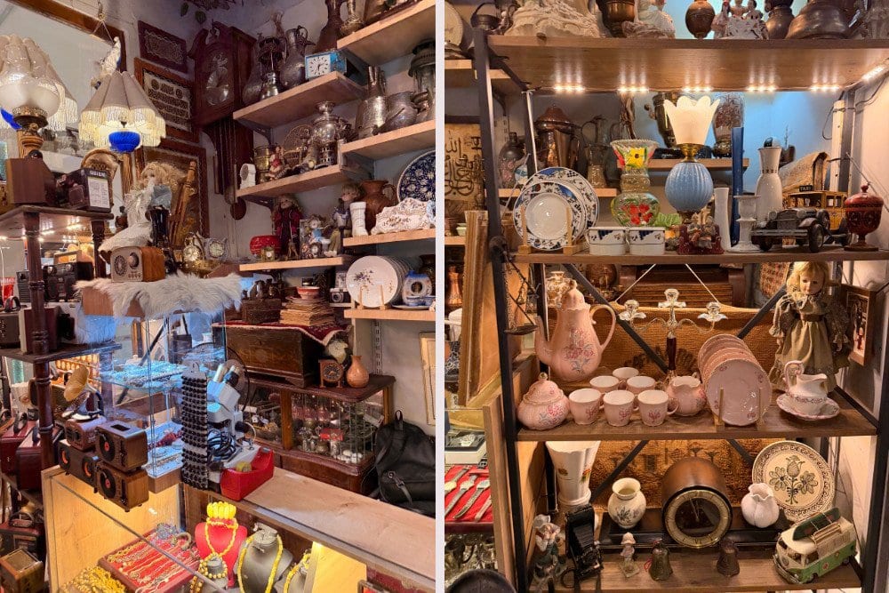 Shelves filled with vintage items, including old cameras, clocks, lamps, ceramics, glassware, and decorative figurines displayed in an antique shop.