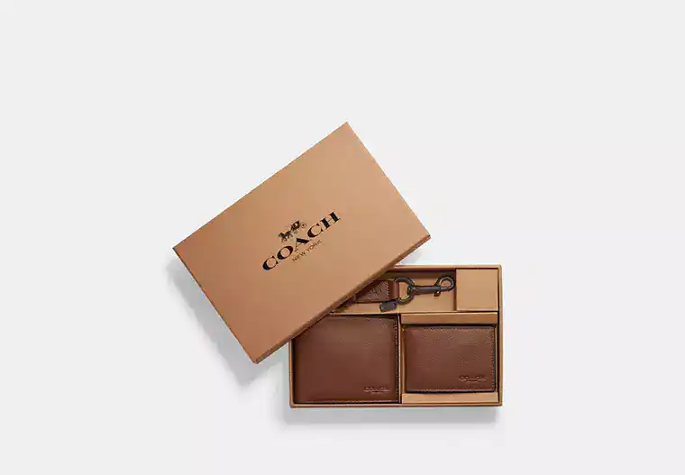 A Coach gift box containing a brown leather wallet, card holder, and keychain on a white background.